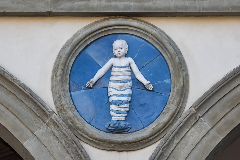 Piazza della Santissima Annunziata, Spedale degli Innocenti, particolare della decorazione della facciata: rilievo in terracotta invetriata che rappresenta un neonato in fasce, realizzato da Andrea della Robbia, 1487.